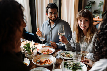 Group of cheerful friends talking and drinking wine while dining in restaurant
