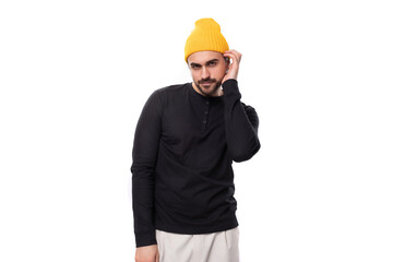 attractive young 30 year old guy with a beard dressed in a black jacket and a yellow hat looks at the camera