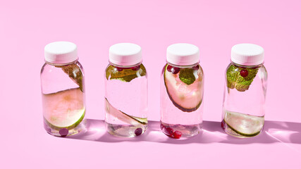 Front view of detox water with cucumber, cranberry, and mint in reusable bottles against a pink backdrop. A modern, minimalist concept of healthy eating