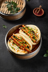Vertical side view of bao buns with tofu and vegetables in a steamer on a black background