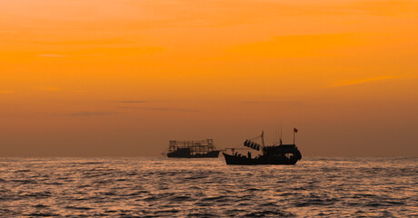 Seascape at dawn with silhouettes of Vietnamese fishermen's fishing boats with yellow-orange light background of Binh Minh. Sea landscape concept and sea work.