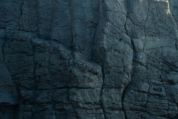 The ancient lava bedrock millions of years ago was on a cliff by the sea, with a contrast of light and dark in the morning sunlight. Black stone nature background, Geological background. Stone concept