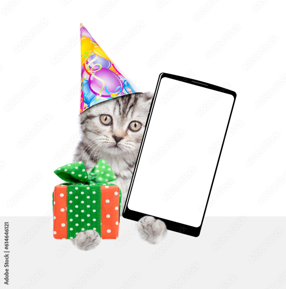 Poster cute kitten wearing party cap holds gift box and shows big smartphone with blank screen above empty 
