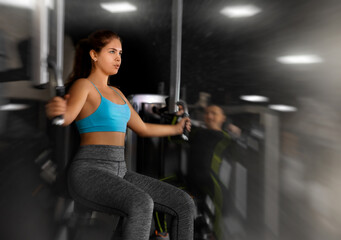 Fototapeta na wymiar Sporty young woman using chest fly machine in gym