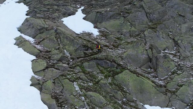 Aerial Footage: Male Mountaineer Hiking on Snowy Rocky Slope with Yellow Jacket in the Alps