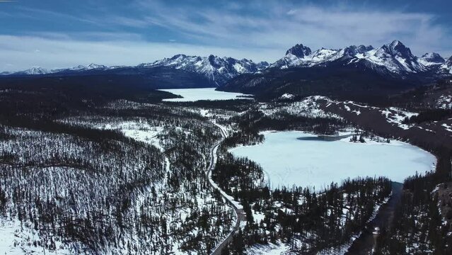 Frozen Redfish Lake Surrounded By Mountains And Forest In Winter Near Stanley In Idaho, USA. wide aerial
