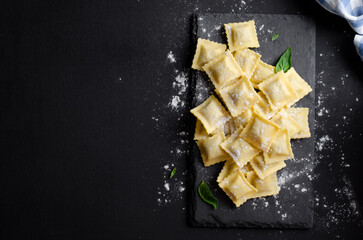 Raw Ravioli with Flour and Basil on Dark Background