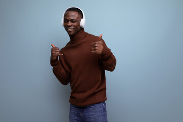 Naklejka premium handsome energetic young african man listening to music with headphones on the background with copy space