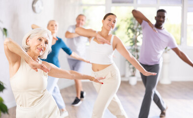 Portrait of elderly woman enjoying active dancing during training with mixed age group in dance studio