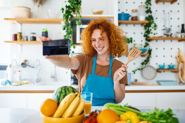 Young woman is in the kitchen, she has wireless headphones on, she is dancing and singing
