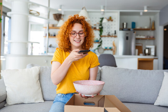 Young satisfied happy woman shopaholic customer sit on sofa unpack parcel delivery box, online shopping shipment concept. taking photos of product to post on social media