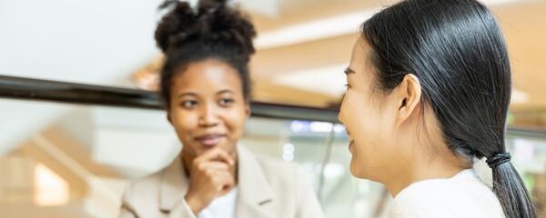 Asian woman talking fluently with her African friend or co-worker, concept image of good command in...