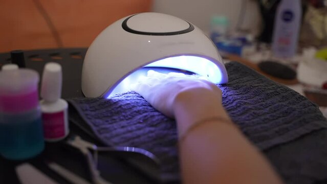 Ultraviolet led lamp used in beauty industry for drying gel nail polish, female hand under the shellac lamp in beauty salon, process of doing trendy gel manicure, art gel nail polish concept