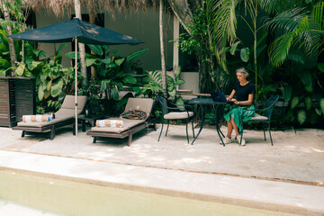 Remote work in tropic country. Woman working with laptop wjile sit in cafe with jungle view, coconut palms around