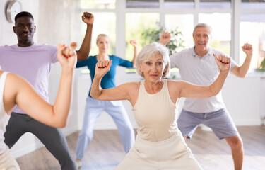 Positive emotional senior woman learning to dance krump with group in modern choreographic studio