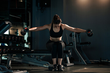 Fototapeta na wymiar Sporty woman lifting dumbbells in the gym.