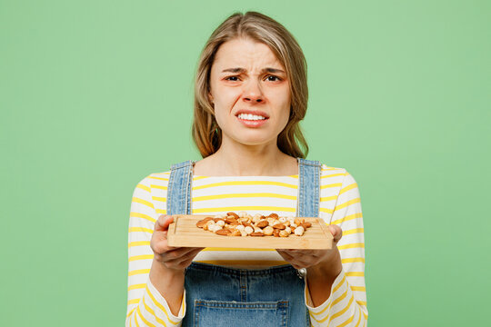 Sick unhealthy allergic dissatisfied woman has red watery eyes runny stuffy sore nose suffer from allergy trigger symptoms hay fever hold peanuts isolated on plain green background studio portrait