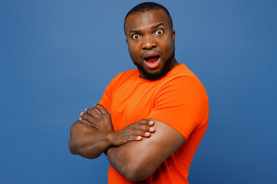 Side view young sad man of African American ethnicity he wear orange t-shirt hold hands crossed folded look camera isolated on plain dark royal navy blue background studio portrait. Lifestyle concept.