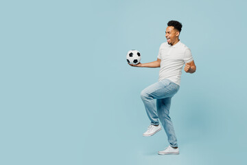Fototapeta na wymiar Full body sideways happy young man fan wear t-shirt cheer up support football sport team hold in hand soccer ball watch tv live stream do winner gesture isolated on plain pastel blue color background.