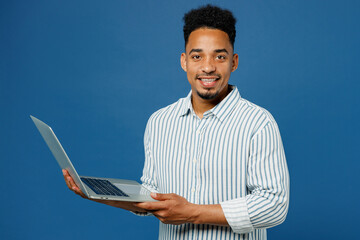 Young happy IT man of African American ethnicity he wear casual clothes shirt hold use work on laptop pc computer isolated on plain dark royal navy blue background studio portrait. Lifestyle concept