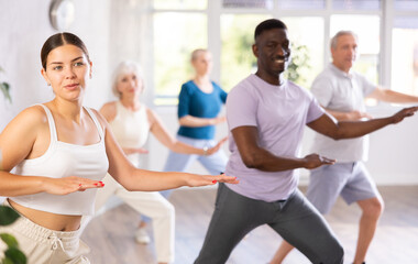 Group of positive young and aged people engaged in sport dances in training room during workout...
