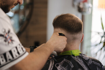 Back view of human hand hold trimmer and make hairstyle for man. Barbershop 