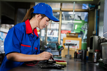 A female diesel engine mechanic in a blue uniform is working at the garage. Inspect and maintain the fuel pressure booster pump system and common rail injectors.