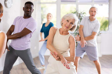 Aged woman takes part in dance class with diverse group of individuals who are enthusiastic about outdoor activities. This multinational group is actively involved in dance lesson and enjoying it.