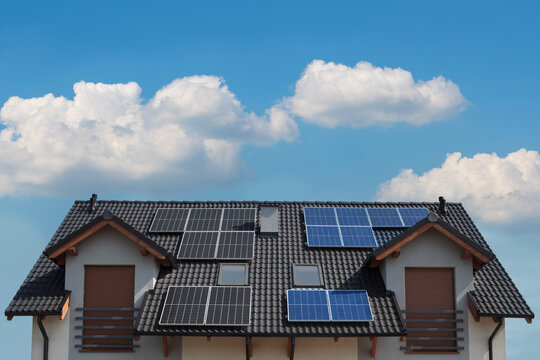 Black and blue solar panels mounted on the roof of a modern house.