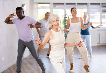 Smiling senior woman dancing vintage twist, popular in sixties, with characteristic arm movements in modern dance studio. Nostalgia for youth. Active hobbies concept