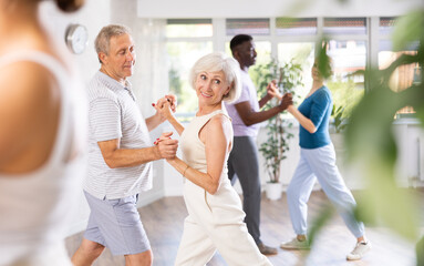 Mature man dances steamy salsa with elderly female companion for fitness classes and enjoys movement and activity. Hobbies, active pastime - obrazy, fototapety, plakaty