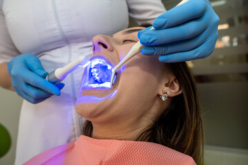 dentist using UV lamp with photopolymer composition for teeth whitening her female patient