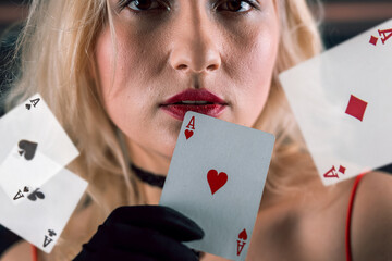 Pretty young woman in red dress and hat holding aces poker card at casino
