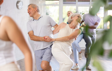 Dynamic mature attendees of dancing courses training Rock and Roll dance poses in dancehall