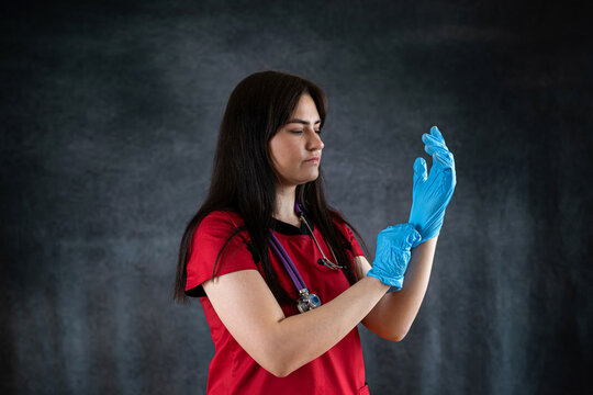 Young Pretty Caucasian Doctor Or Nurse In Red Uniform Putting On  Latex Gloves Isolated On Black