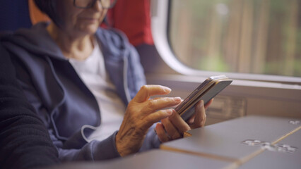 Fototapeta premium Close-up of the hands of an elderly woman sitting in a train carriageriage and using a smartphone