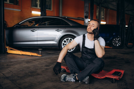 Handsome young mechanic talking to a customer on a cellphone while working on a computer at an auto shop.