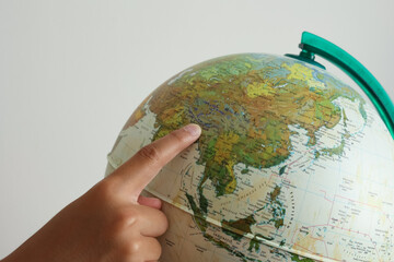 A boy's finger pointing China map on a white and green model earth globe ball.