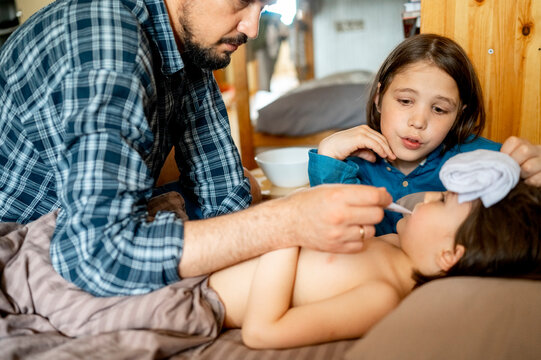 Father checking temperature of sick son with thermometer at home