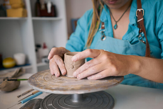 Craftswoman sculpting clay cup on pottery wheel at workshop