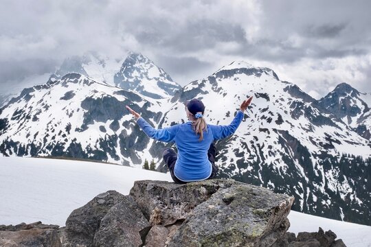 Woman in yoga pose meditating in frot of snow capped mountains on rock. Colorado. USA