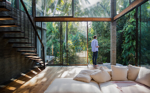 Thoughtful young man standing by glass door at home