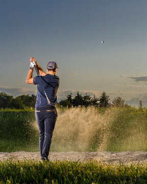 Man hitting golf ball on grass at dusk