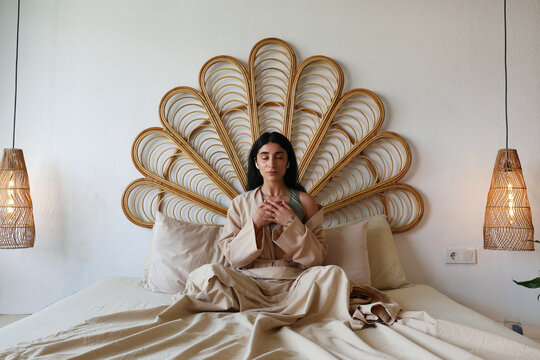 Young Woman Meditating Sitting On Bed At Home