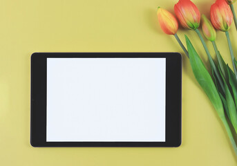 flat lay of digital tablet with blank white screen, tuip flowers  isolated on yellow background.