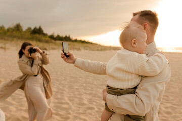 Father taking selfie with son and woman photographing through camera at beach
