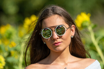 pretty sensual young brunette in sunglasses in a field of blooming sunflowers, young woman portrait