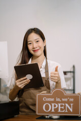 Fototapeta premium Startup successful small business owner sme beauty girl stand with tablet in her coffee shop. Portrait of asian woman barista cafe owner. SME entrepreneur business concept.