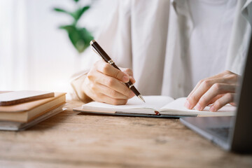 Male sitting at a table at home working on a laptop and writing down ideas in a notebook.