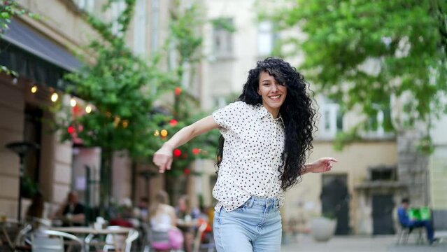 Happy young woman dancing on the city street. Cheerful Curly Attractive Pretty Female dancer Enjoying Life, Happiness Joy urban Lifestyle Concept. Beautiful Cute funny Girl look at camera outdoor